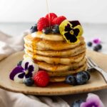 a plate served with pancakes, berries, yogurt, flowers, and maple syrup