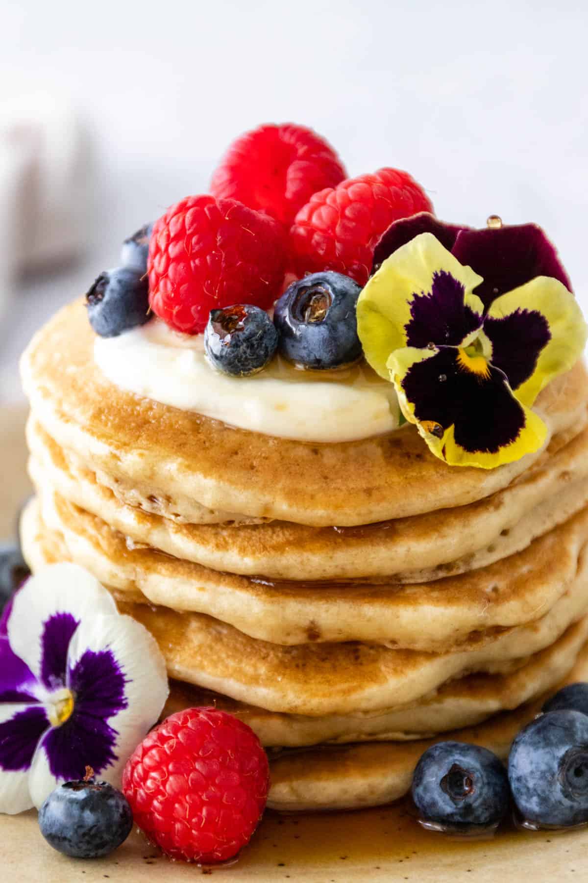 close up to a batch of pancakes with yogurt, maple syrup, berries, and flowers