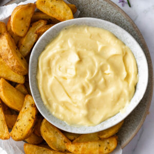 a small bowl with aioli with potato wedges on the side