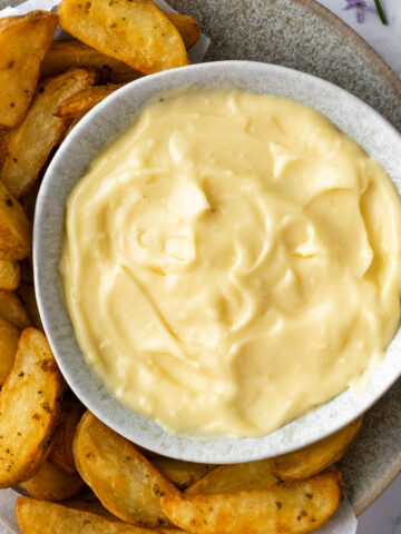 a small bowl with aioli with potato wedges on the side