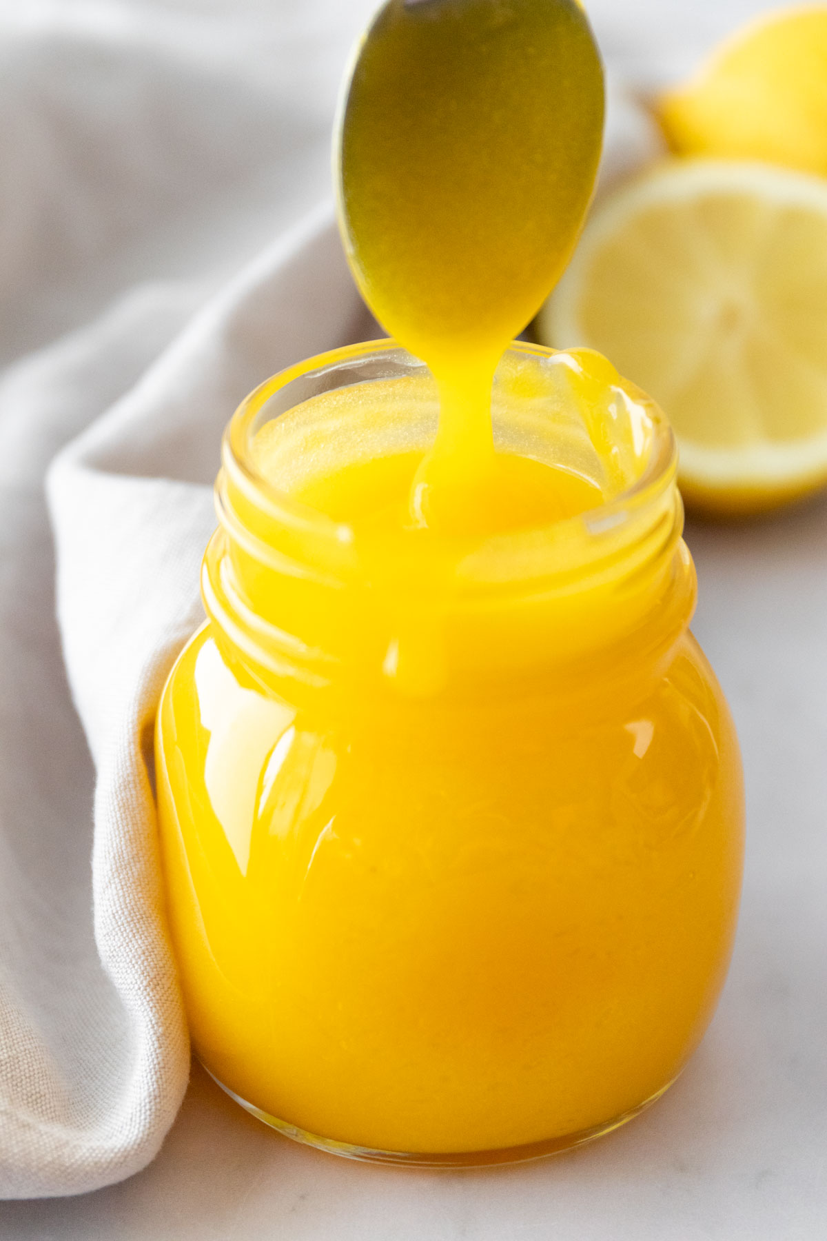 a small jar with lemon curd and a spoon with a drizzle of lemon curd on the top