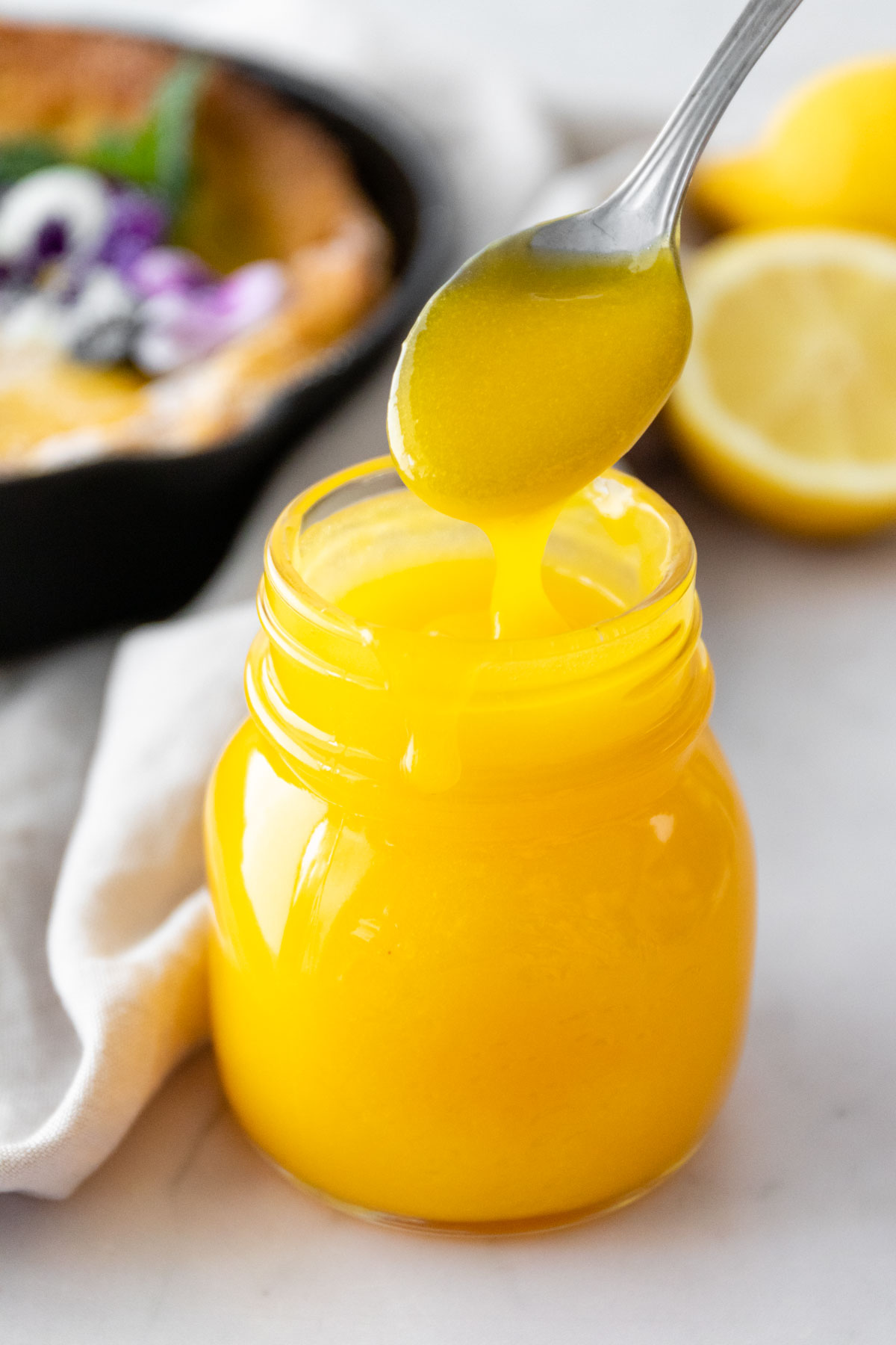 a small jar with lemon curd and a spoon with a drizzle of lemon curd on top