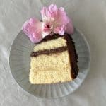 vanilla sponge cake slice with chocolate frosting and a flower on a plate